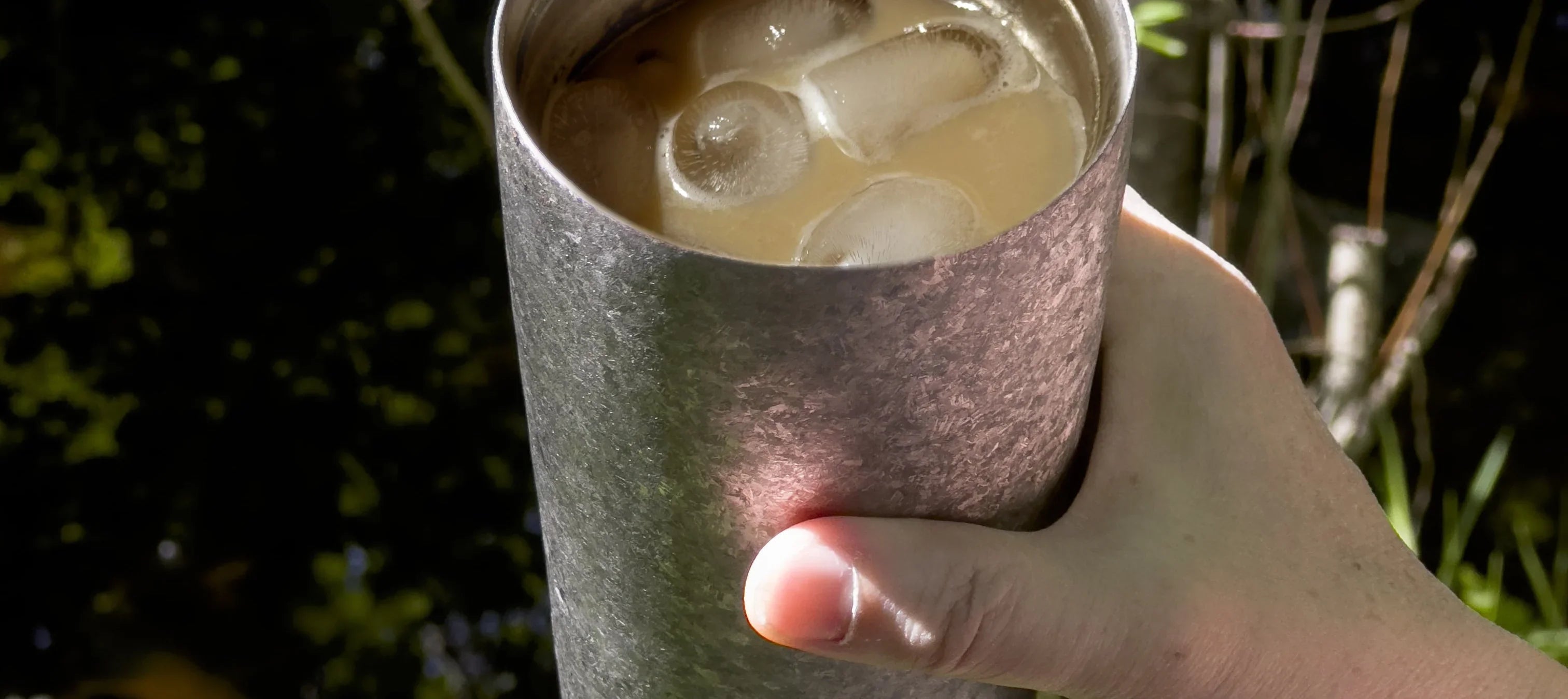KOYASU 17oz Whole-Body Titanium Mug – handheld with iced coffee outdoors, lightweight hiking tumbler