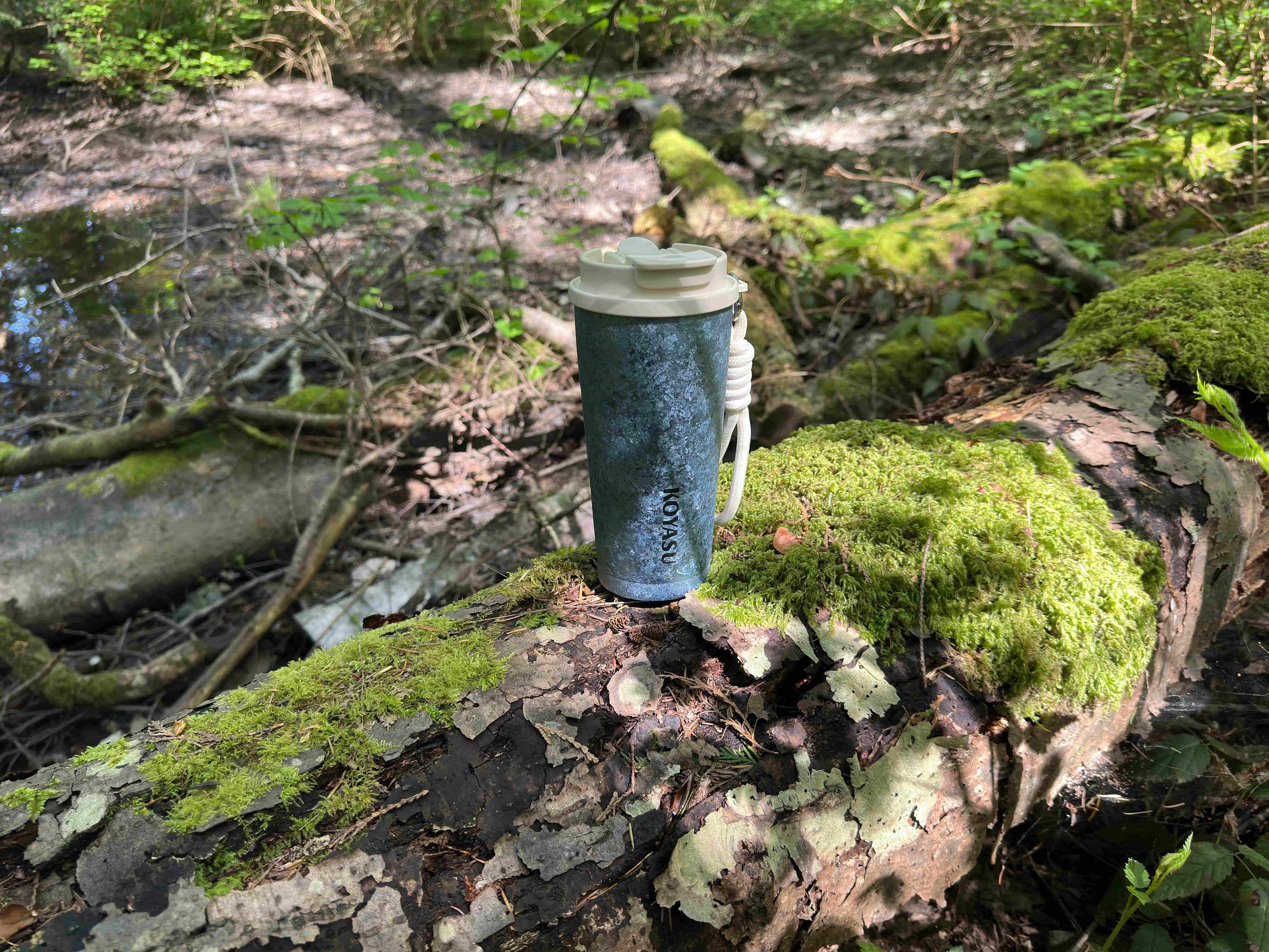 KOYASU® Ti-Zero™ 16oz pure titanium coffee mug held by hand on a misty forest trail. Ultralight, double-wall vacuum insulated travel tumbler with raw crystal titanium texture for camping, hiking, and outdoor adventures.