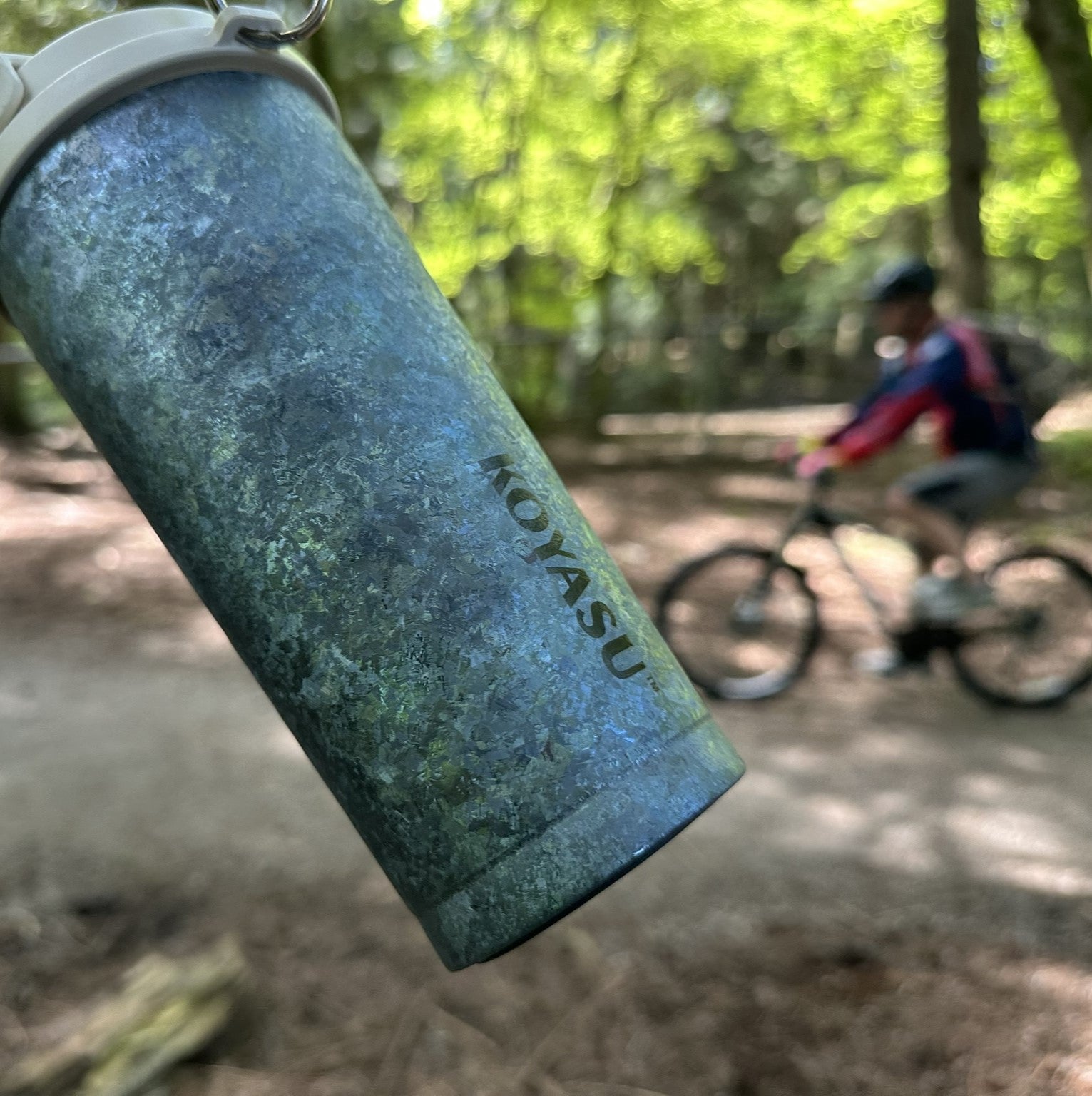 KOYASU whole-body titanium mug hanging outdoors with biker in background, ideal for hiking and camping
